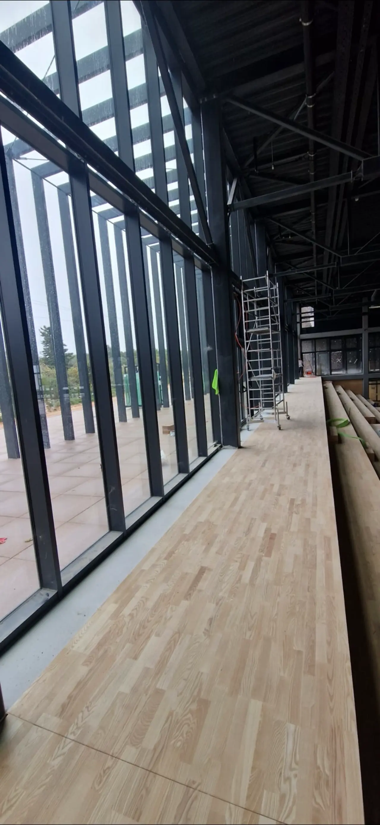 Čišćenje i održavanje modernog interijera s velikim staklenim stijenama i drvenim podovima u sportskom objektu.